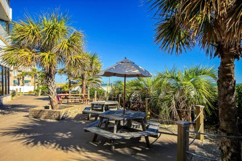 a picnic table and benches with an umbrella and palm trees at Sands Ocean Club 1630 in Myrtle Beach