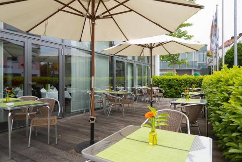 an outdoor patio with tables and chairs and umbrellas at Corbin München Airport Business Hotel in Freising