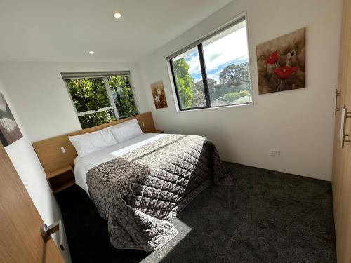 a bedroom with a bed and two windows at Plymouth Central City 2 Bedroom Apartments in New Plymouth