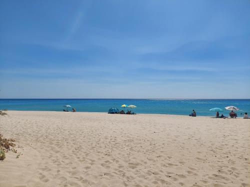 a group of people sitting on a beach with umbrellas at SU BISU Costa Rei R4991 terrace with sea view, 500m from the beach in Costa Rei