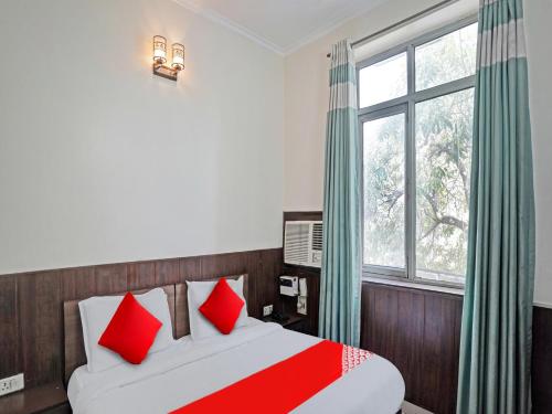 Schlafzimmer mit einem Bett mit roten Kissen und einem Fenster in der Unterkunft Hotel Grand Stay in Ghaziabad