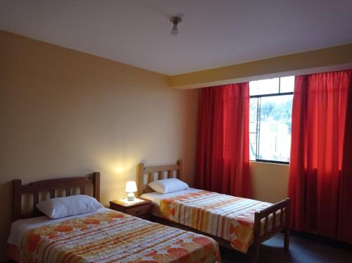 two beds in a room with red curtains and a window at Hostal Madrid in Pisco