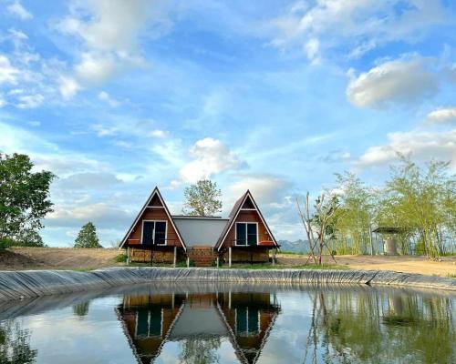 a house with a pond in front of it at บ้านไร่ชายทุ่ง in Kanchanaburi