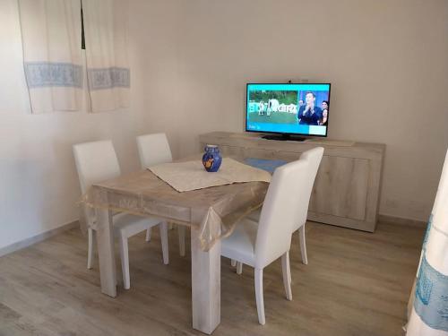 a dining room table with white chairs and a television at LA Pavoncella in La Maddalena