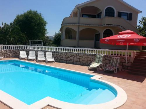 a swimming pool with chairs and an umbrella next to a house at Apartments Dedić in Supetarska Draga