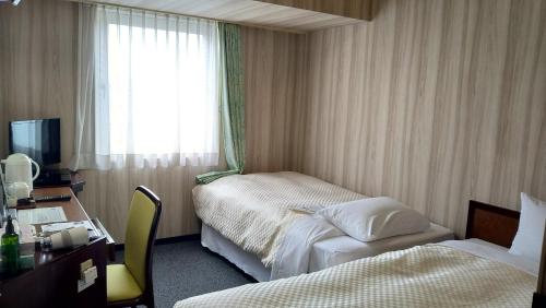 大館市にあるロイヤルホテル大館のベッド2台、デスク、窓が備わるホテルルームです。