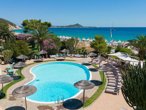 uma vista para uma piscina com guarda-sóis e para o oceano em Cormoran Hotel em Villasimius