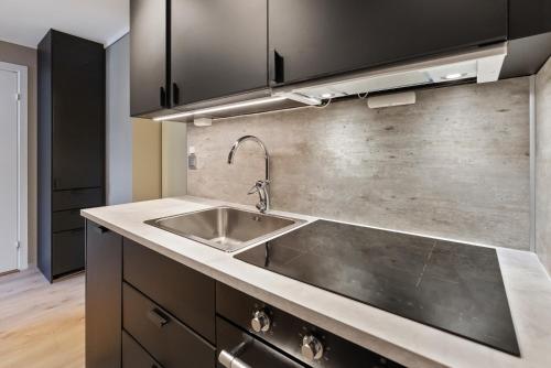 a kitchen with a stainless steel sink and black cabinets at Ny sentral og moderne leilighet in Kristiansand
