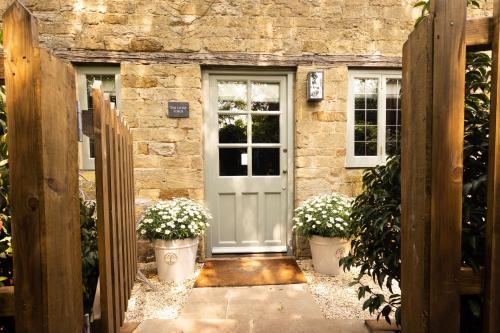 a stone house with a white door and two potted plants at Cotswold cottage with hot tub in Bledington