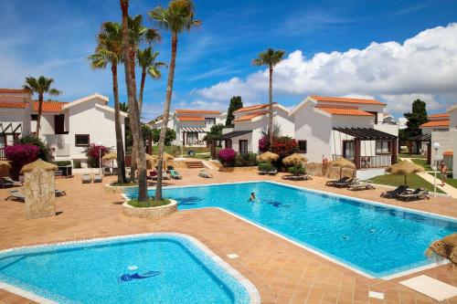 a large swimming pool with palm trees in front of a house at Nuramar Resort & Villas in Cala'n Bosch