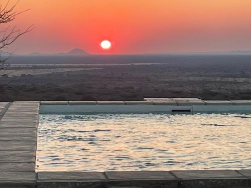 a swimming pool with a sunset in the background at Aloegrove Safari Lodge in Otjiwarongo