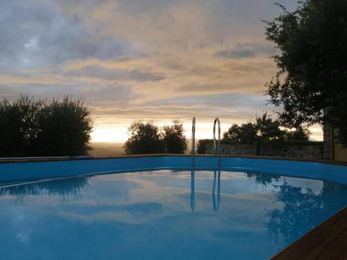 une piscine bleue avec un coucher de soleil en arrière-plan dans l'établissement Vecchio Casale Quercetino - Il forno, à Montenero