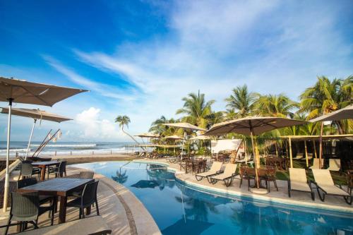 a resort pool with tables and umbrellas and the ocean at Mishol Bodas Hotel & Beach Club Acapulco Diamante in Acapulco