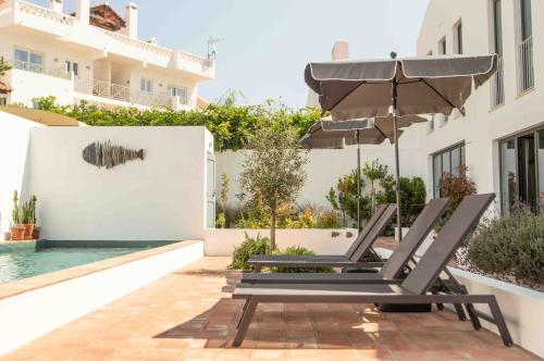 a pair of lounge chairs under an umbrella next to a pool at Vida na Vila in Vila Nova de Milfontes