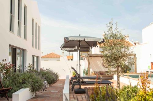 a patio with an umbrella and chairs and a boat at Vida na Vila in Vila Nova de Milfontes