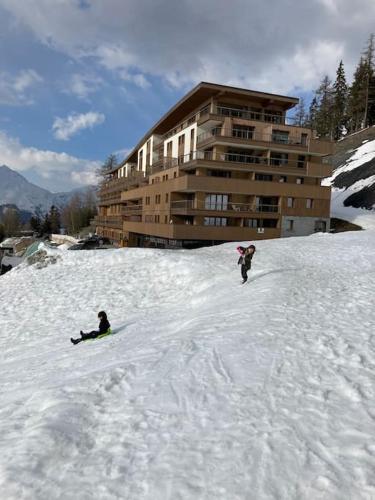 two people on snowboards in the snow in front of a building at Luxurious duplex for 4-7p with large terrace and pool in ski-in ski-out 5 star residence at Les Arcs in Bourg-Saint-Maurice