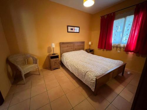 a bedroom with a bed and a chair and red curtains at Finca Los Molinos in La Alameda de Cervera