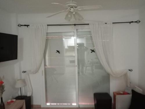 ein Fenster mit weißen Vorhängen und einem Deckenventilator in der Unterkunft Apartamento HAKUNA MATATA con gran terraza, planta baja in Playa de San Juan