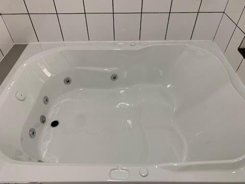 a white bath tub in a bathroom with white tiles at 24 Horas Motel Jaguar Contagem in Contagem