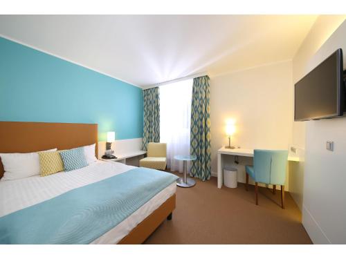 a bedroom with a bed and a desk with a computer at Congress Hotel am Stadtpark in Hannover