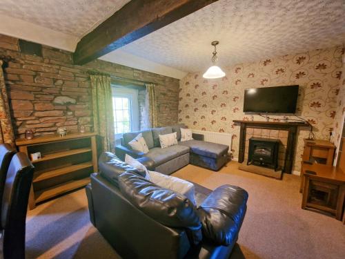 a living room with a leather couch and a fireplace at Windale at Wetheral Cottages in Great Salkeld