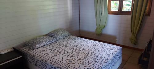 ein kleines Bett in einem Zimmer mit einer Bettdecke und einem Fenster in der Unterkunft Enzo lodge chambre hibiscus in Papawa