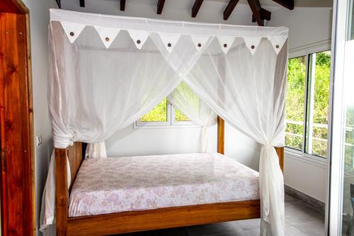 a bedroom with a canopy bed with a window at Villa Grenade (haut) - Vue mer et Fort-De-France in Sainte-Luce