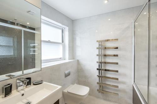 a bathroom with a toilet and a sink and a window at High Street Kensington Apartment in London