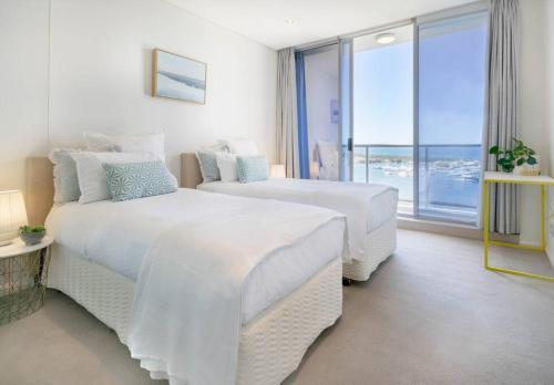 a white bedroom with two beds and a large window at Southport Sea Views - Shores Apartment in Gold Coast