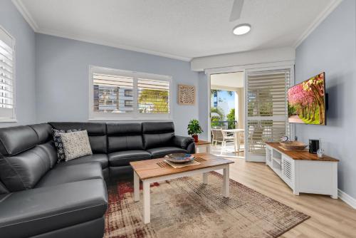 a living room with a black leather couch and a table at Raffles Mooloolaba in Mooloolaba