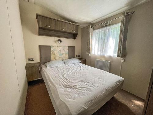 Un pequeño dormitorio con una cama blanca y una ventana en Lovely 8 Berth Caravan With Decking And Nearby Scratby Beach Ref 50005a en Great Yarmouth