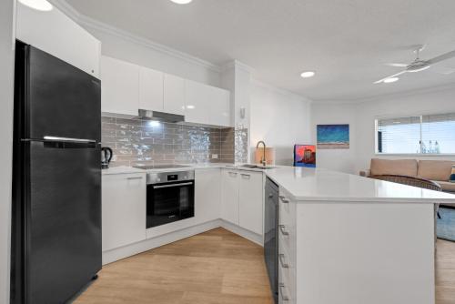 a kitchen with white cabinets and a black refrigerator at Raffles Mooloolaba in Mooloolaba