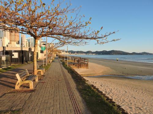 a brick sidewalk next to a beach with benches at Apart moderno 3 suites 2 vagas de garagem e quadra do mar in Itapema