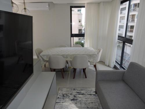 a living room with a table and chairs and a television at Apart moderno 3 suites 2 vagas de garagem e quadra do mar in Itapema