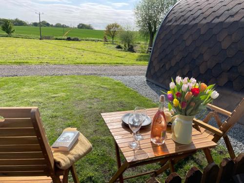 a wooden table with flowers and a bottle of wine at Waterpump Pod for 2 adults with ensuite in the Suffolk Countryside in Badingham