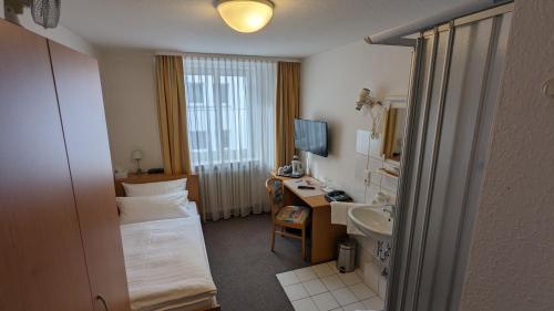 シュトゥットガルトにあるゲストハウス ツィグラーのベッド、デスク、シンクが備わるホテルルームです。