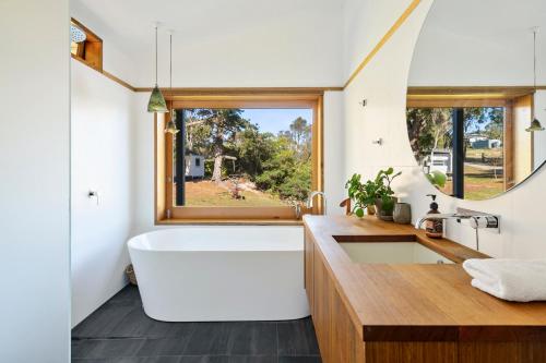 baño con bañera grande y ventana en 'Questa' Heritage Cottage, en Barnes Bay