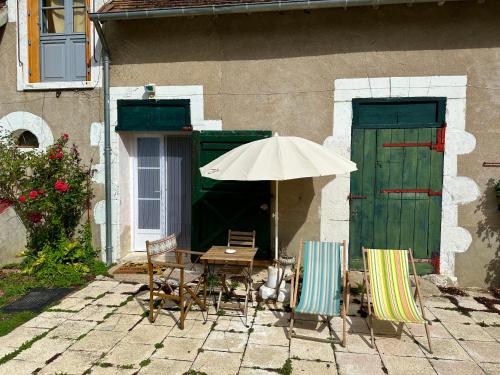 uma mesa e cadeiras com um guarda-sol em frente a um edifício em La maison des rosiers au bord du Loir 