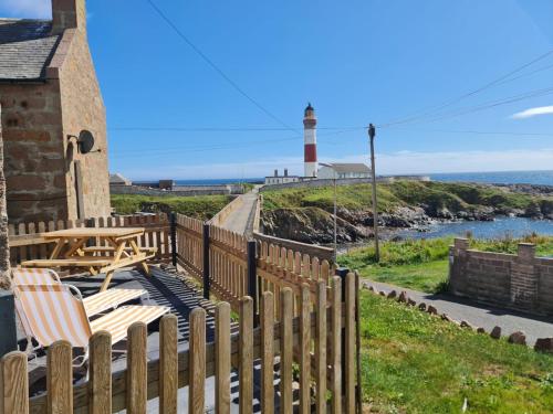 uma cerca de madeira com duas cadeiras e um farol em Puffin Cottage em Boddam