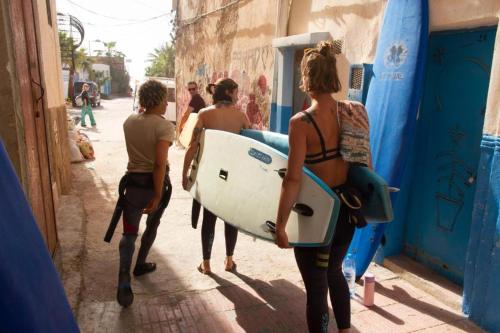 un grupo de personas caminando por una calle sosteniendo tablas de surf en Slimo, en Sidi Ifni