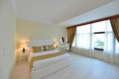 a white bedroom with a bed and a large window at Te Stela Resort & SPA in Tirana