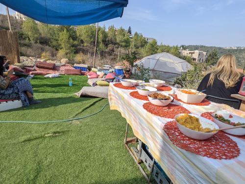 einen Tisch mit Schüsseln Essen auf dem Rasen in der Unterkunft אשראם בכרמל - אכסניה in Dāliyat el Karmil