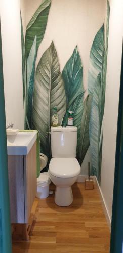 La salle de bains est pourvue de toilettes et d'une fresque murale représentant des feuilles. dans l'établissement Gîte une histoire de village, à Genneteil