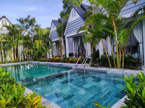 a swimming pool in front of a house with palm trees at Ngoc Trai Xanh Bungalow in Phú Quốc