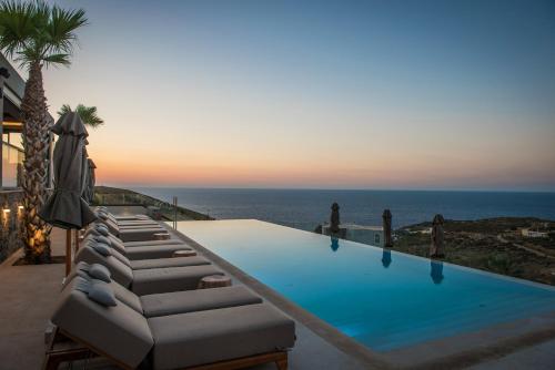 a swimming pool with lounge chairs and the ocean at Happy Cretan Suites in Agia Pelagia