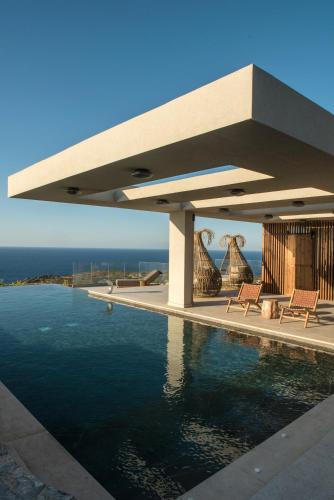 a swimming pool next to a house with the ocean at Happy Cretan Suites in Agia Pelagia