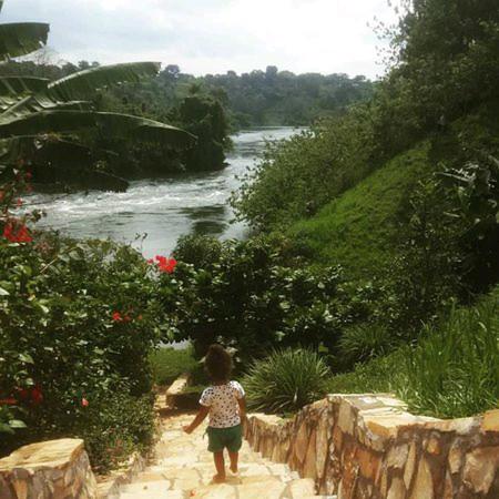 uma menina caminhando por um caminho ao lado de um rio em Nileit Campsite Jinja em Jinja