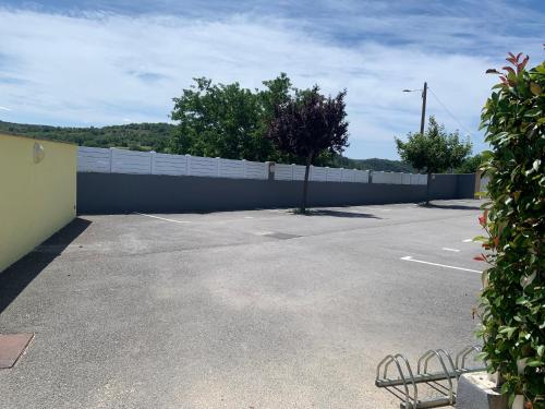 a parking lot with a white fence and trees at Aux couleurs d’Ardèche in Vallon-Pont-dʼArc