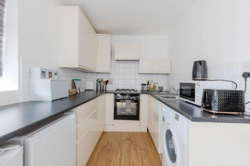 Near Wembley, beautiful apartment with garden, self check-in في لندن: مطبخ بدولاب أبيض وقمة كونتر أسود