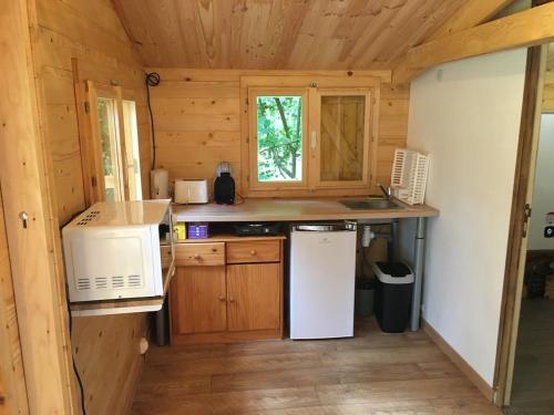 a kitchen in a log cabin with a microwave and a refrigerator at Cabane au milieu des bois in Lanvellec